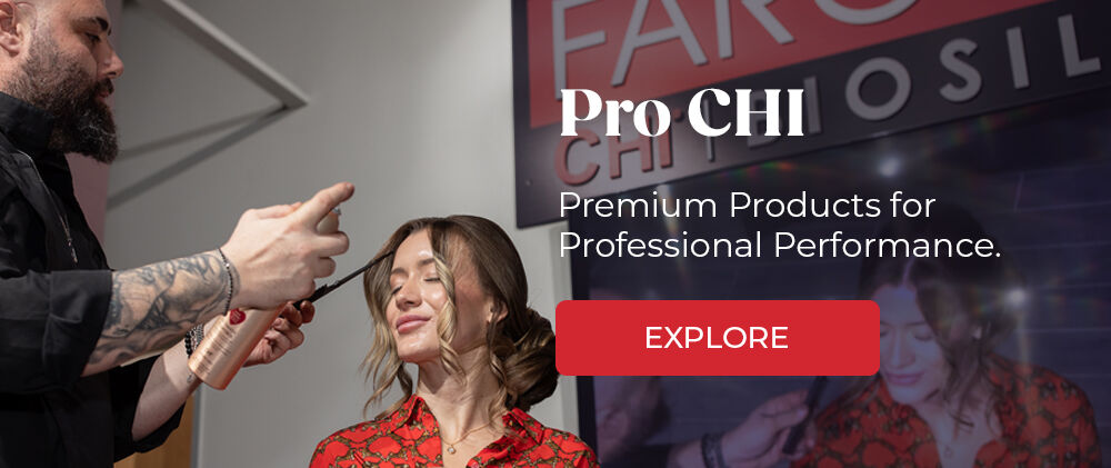 Bearded man spraying a seated model's hair with CHI hair spray.